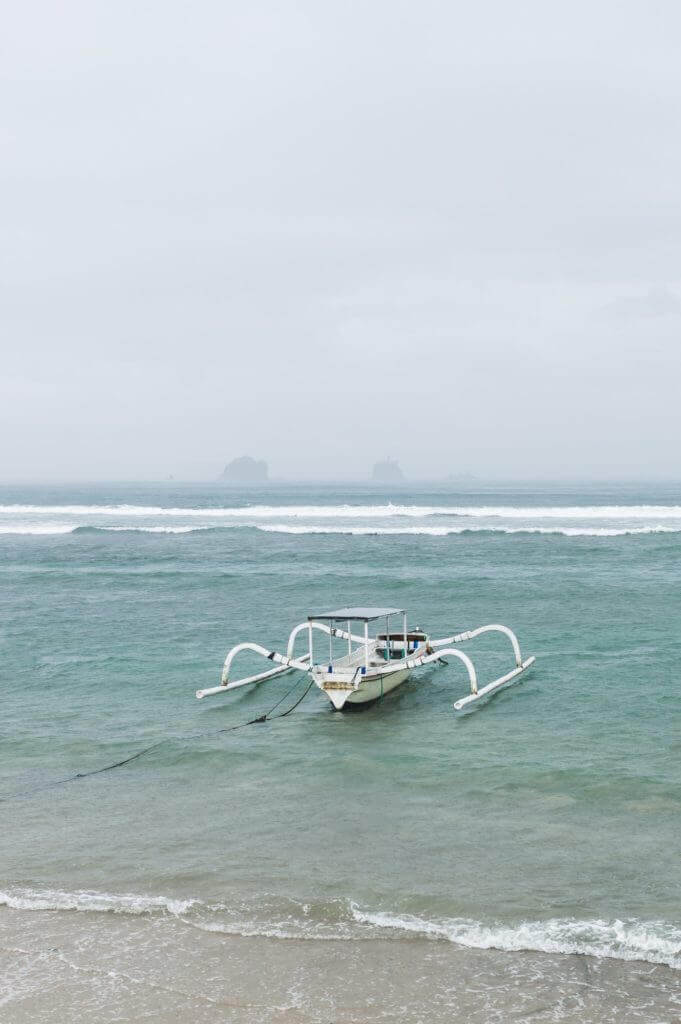 One White Traditional Bali Fishing Boat On Big Waves In Storm And Raining Candidasa Beach E1625712192429 681x1024